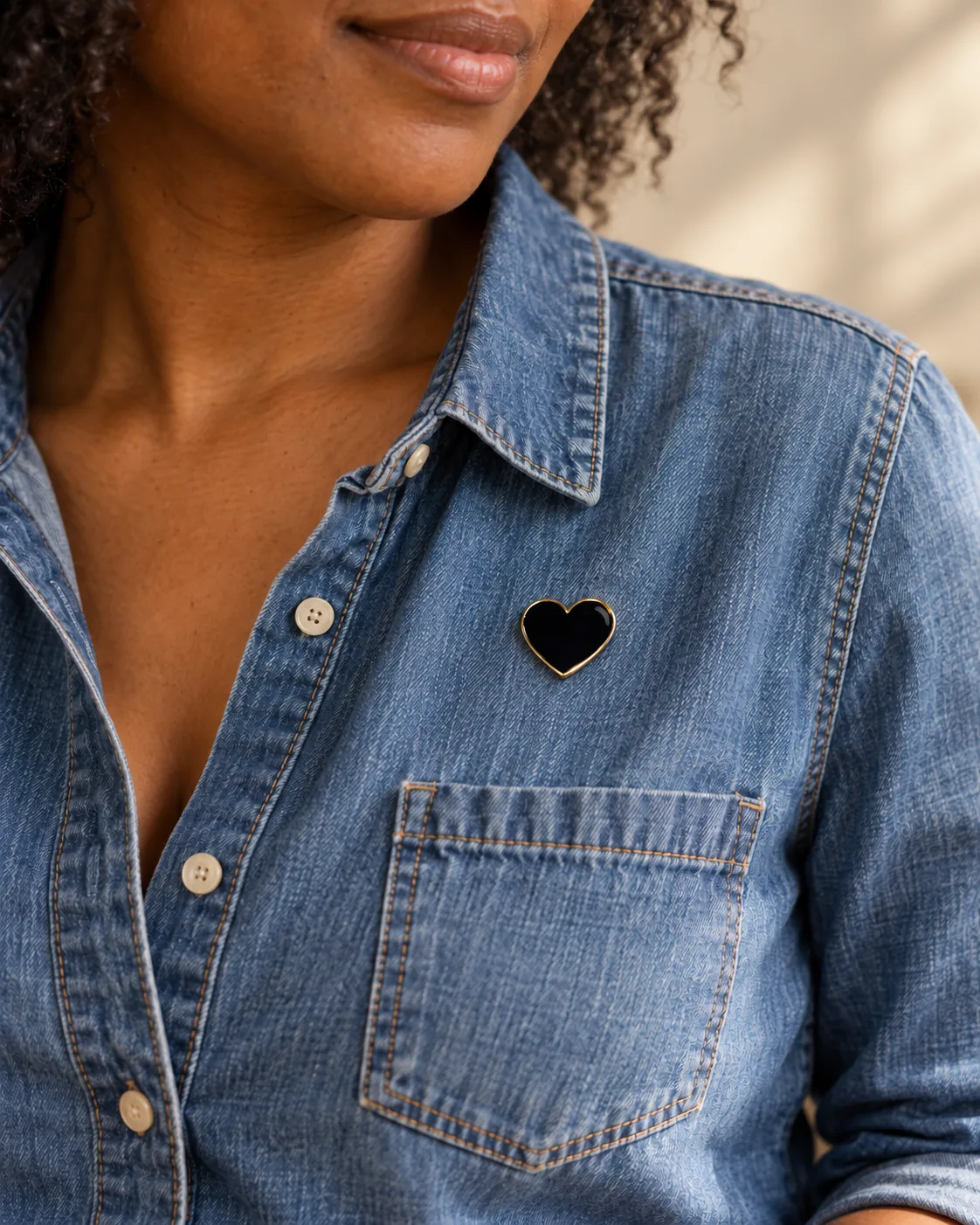 A black enamel Mourning Heart pin with gold trim worn on a denim shirt